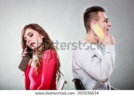 Young couple talking on mobile phones sitting back to back. Pensive woman and thoughtful man making a call. Wife and husband bored with relationship. Communication concept. Studio shot.