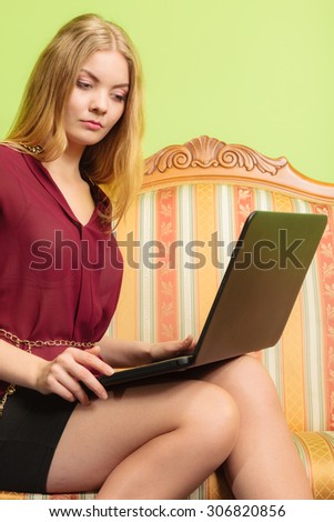 Young fashionable woman girl sitting on vintage retro sofa couch using laptop computer surfing the internet. Fashion and modern technology.
