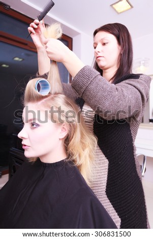 Beautiful young woman in beauty salon. Blond girl with hair curlers rollers by hairdresser. Hairstyle.