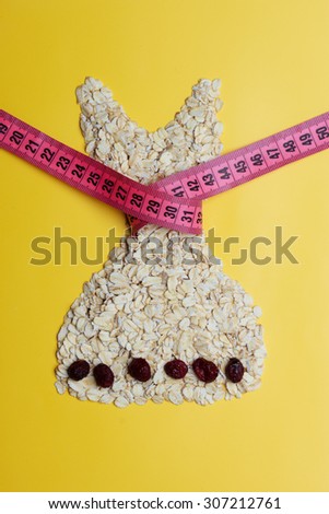 Dieting healthy eating slim down concept. Female dress shape made from oatmeal dried fruit with measuring tape around thin waist on yellow