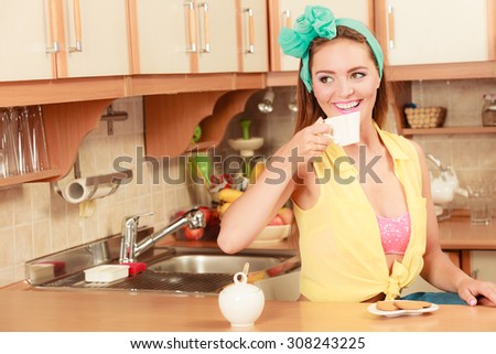 Pretty pin up girl with heart shape gingerbread cookies drinking tea or coffee at home. Gorgeous young retro woman with hot beverage relaxing in kitchen.