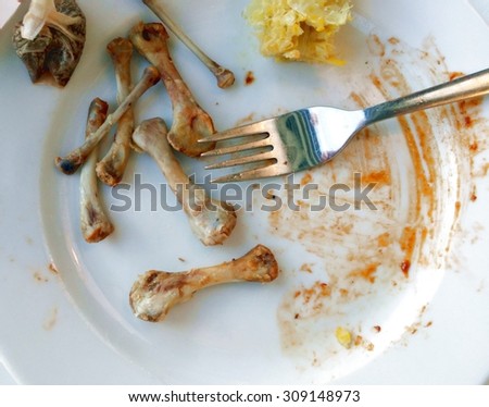 Food leftovers. Dirty plate with chicken meat bones after the meal is finished.