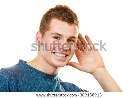 Gossip. Young man holding hand to ear listening isolated on white background
