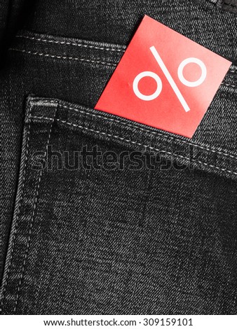 Shopping and sale concept. Closeup red label with percent sign on black jeans pocket denim cotton material background