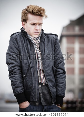 Young handsome freezing man fashion model casual style on street urban industrial background. Cold foggy day