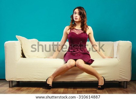 Fashion young woman in full length. Girl in fashionable dress high heels sitting on couch vivid color blue background