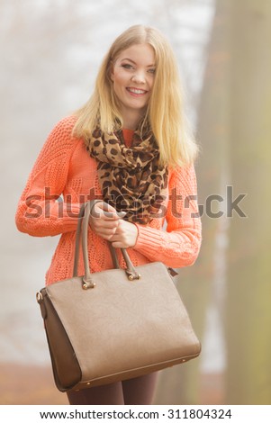 Happy fashionable woman in foggy autumn park. Pretty young girl with handbag in forest. Fall fashion vogue.