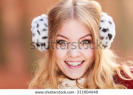 Portrait of pretty smiling fashionable woman in fall forest park. Happy gorgeous young girl in fur earmuffs. Autumn winter fashion.