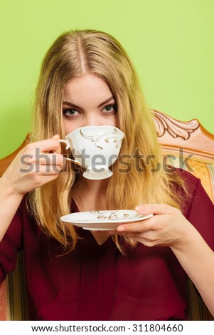 Fashionable woman drinking cup of coffee sitting on vintage sofa. Young girl with hot energizing beverage stay awake. Caffeine energy.