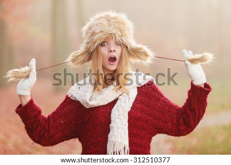 Portrait of surprsied amazed pretty fashionable woman in fall forest park. Gorgeous young girl in fur winter hat and sweater pullover. Autumn fashion.