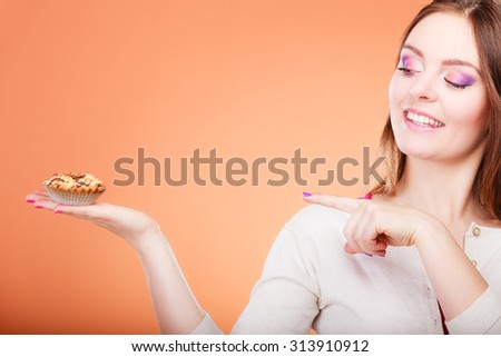 Bakery sweet food and people concept. Smiling woman holds cake cupcake in hand pointing with finger orange background