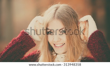 Portrait of pretty smiling fashionable woman in fall forest park. Happy gorgeous young girl in earmuffs and sweater pullover. Autumn winter fashion.