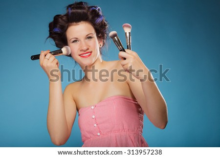 Cosmetic beauty procedures and makeover concept. Woman in hair rollers holding makeup brushes set on blue