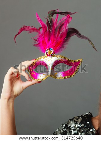 Holidays, people and celebration concept. Closeup woman hand holding carnival venetian mask on gray background.