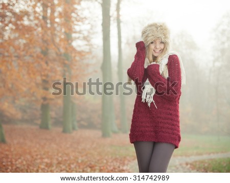 Portrait of pretty smiling fashionable woman in fall forest park. Happy gorgeous young girl in fur winter hat and sweater pullover. Autumn fashion.