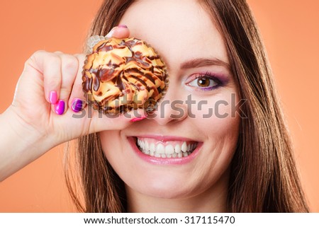 Diet sweet food and people concept. Funny woman holds cake in hand having fun covering her eye with cupcake orange background