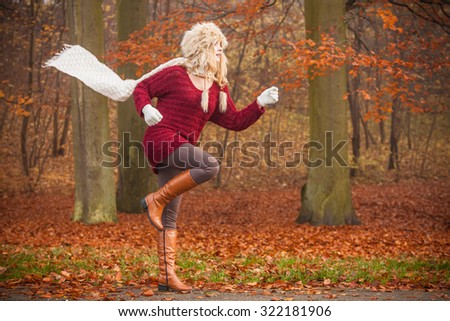 Fashion woman with flying scarf running in fall autumn park forest against blowing wind. Girl in fur cap having fun.