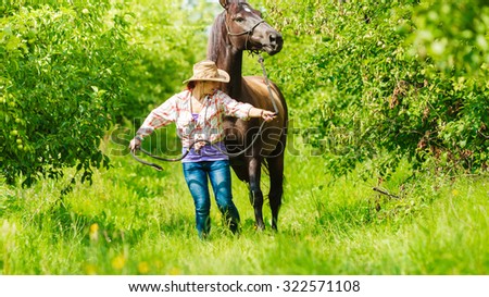 Active western cowgirl woman in hat walking with horse. American girl in countryside ranch.