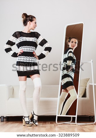 Fashion and shopping. Woman trying dress sweater choosing clothing. Attractive female shopper looking in mirror, standing in clothes store.