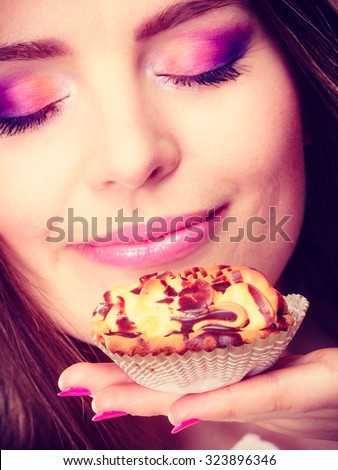 Bakery sweet food and people concept. Content attractive woman closed eyes holds cake cupcake in hand smelling orange background