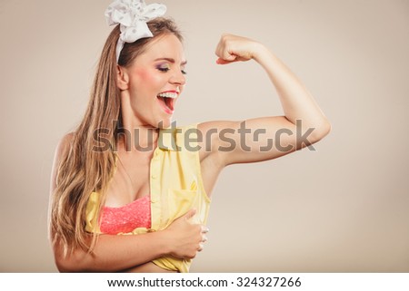 Happy strong pretty pin up girl with hairband bow showing off muscles. Young gorgeous retro woman in studio.