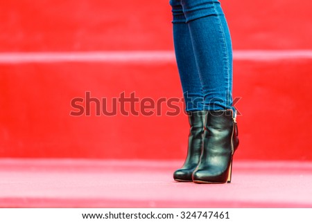Autumn fashion outfit. Fashionable woman long legs in denim pants black stylish high heels shoes outdoor on red steps