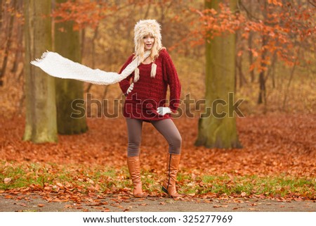 Joyful fashion woman with flying scarf in windy fall autumn park forest against blowing wind. Young girl in fur cap and sweater having fun outdoor.