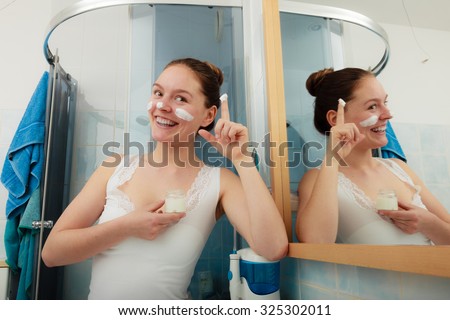 Happy young woman applying cleansing moisturizing skin cream on face. Girl taking care of dry complexion layering moisturizer. Skincare.