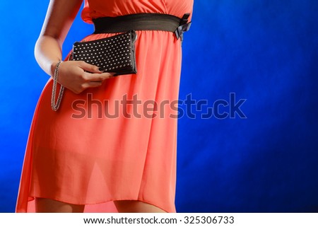 Fashion elegant evening outfit. Female hand holding black rivet leather handbag clutch bag on blue background