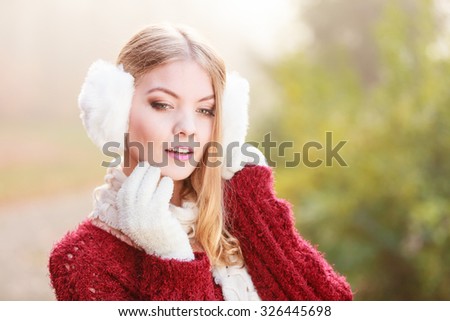 Portrait of pretty attractive fashionable woman in fall forest park. Gorgeous young girl in white fur earmuffs and maroon sweater pullover. Autumn winter fashion.