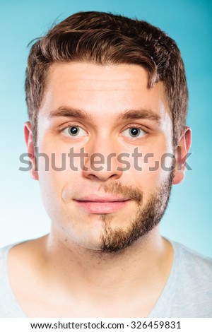 Portrait of young man with half shaved face beard hair. Handsome guy on blue. Skin care and hygiene.