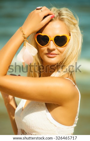 Holidays, vacation and summer fashion concept. Closeup attractive blonde girl in orange heart shaped sunglasses outdoor on beach water background