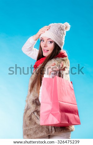 Winter woman in warm clothes with red paper shopping bag on blue. Girl buying. Sale and retail.