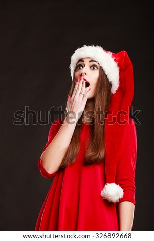 Christmas time. Young woman wearing santa claus hat red dress on black background. Surprised face expression.