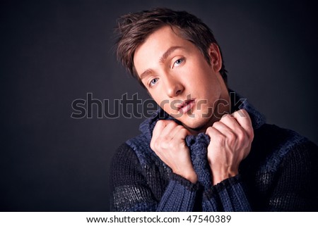 handsome young man raised the collar blue sweater on a black background