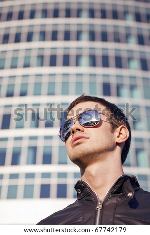 a young man in sunglasses looking up at skyscraper windows background
