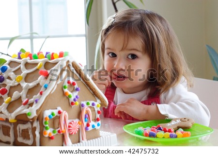 Little girl decorating gingerbread house and treating herself to candy