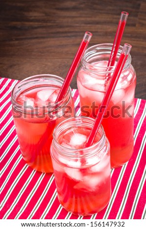Three mason jars in different sizes and shapes with ice, drinks and a straw. This is home made ice tea, but could just as well be lemonade.