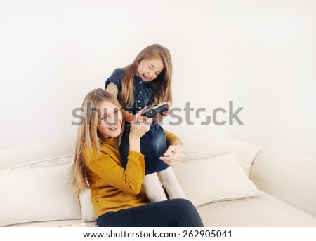little girl with her mother playing TV video game device on the sofa at home, happy family, technology concept