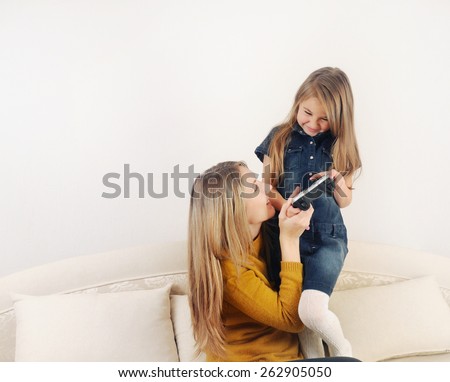 little girl with her mother playing TV video game device on the sofa at home, happy family, technology concept
