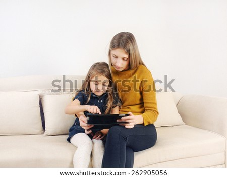 little girl with her mother using tablet device on the sofa at home, happy family, technology concept