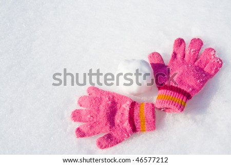 Warm female pink gloves and snowball on fresh snow.