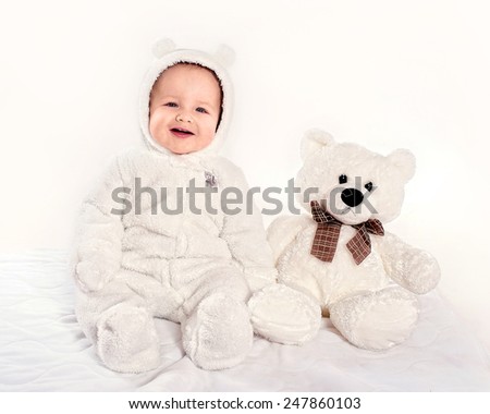 the little boy in a suit of a bear cub sits near a teddy bear on a light background