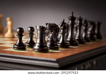 Left flank of the black army of luxurious chess pieces in focus on a wooden chessboard with dark background