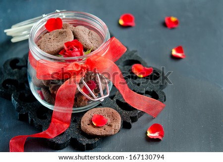 Chocolate chip cookies on a dark wooden table and a red rose