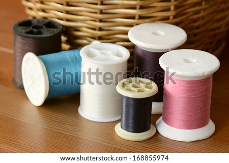 Colored spools of cotton threads on wooden surface and woven basket background