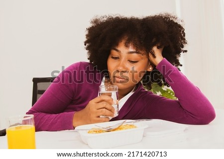 Portrait black african american teenage girl holding glass of water sitting looking lunchbox unpalatable fried eggs and bland rice less nutrition unhappy to eat not wanting to eat and not interested. Stock foto © 