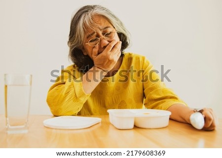 Unhappy elderly asian woman sits and eats prepackaged food in plastic boxes that are monotonous and unpalatable covers her mouth with her hands does not want to eat is bored. Stock foto © 