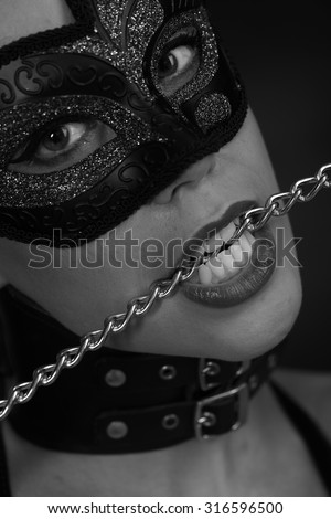 Woman in a mask holding a chain in his mouth