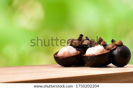 Mangosteen on the wooden table edge with blurred green forest as a background. Five mangosteens, two of them was peeled that reveal white flesh and the other that behind doen't peel. Queen of fruits. Stockfoto © 